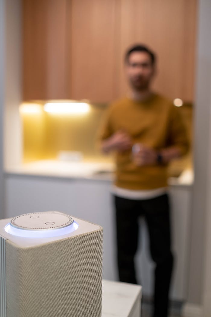 Blurred man commands a wireless smart speaker in a contemporary kitchen setting.